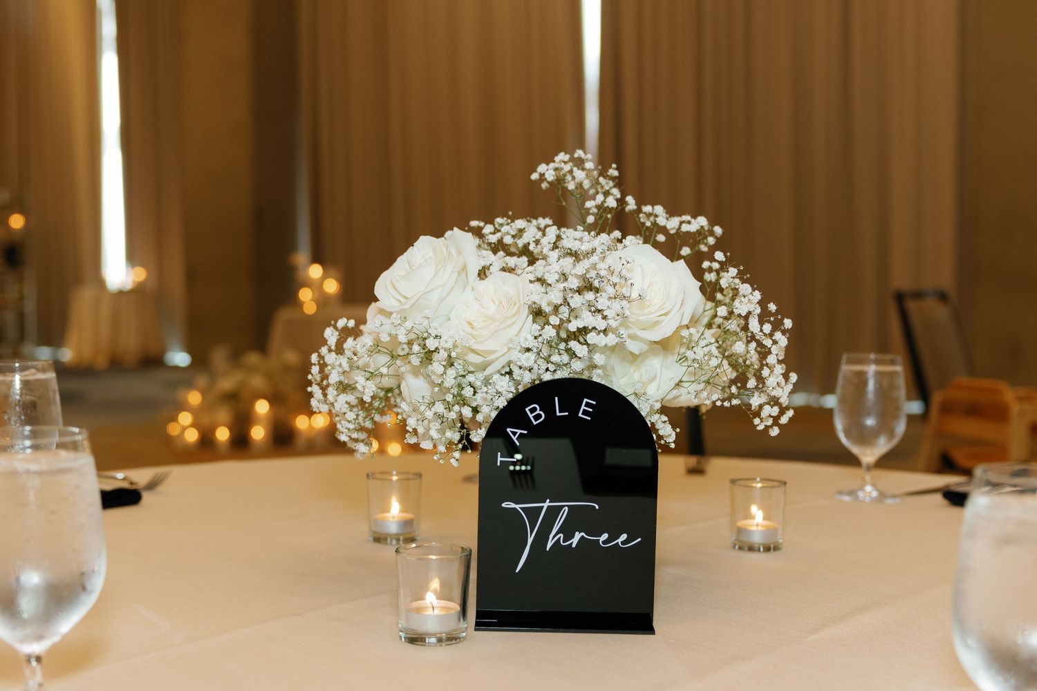 White floral centerpiece arrangements with baby's breath on tables at an elegant wedding reception.