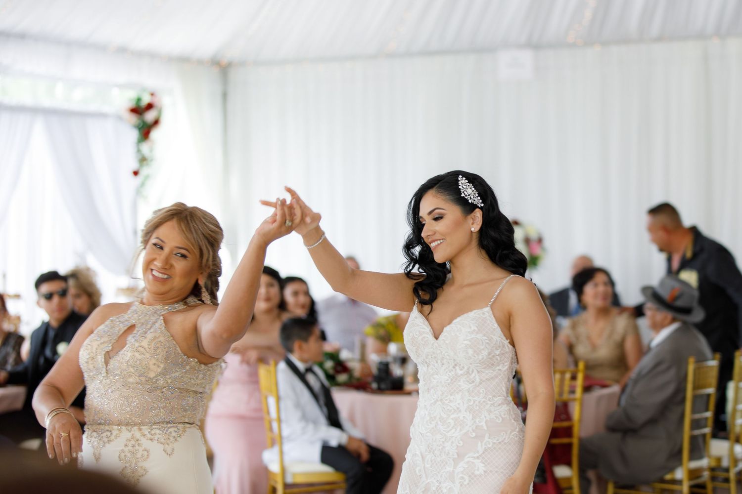 A group of wedding guests dance and celebrate together under a white tent at an outdoor reception.