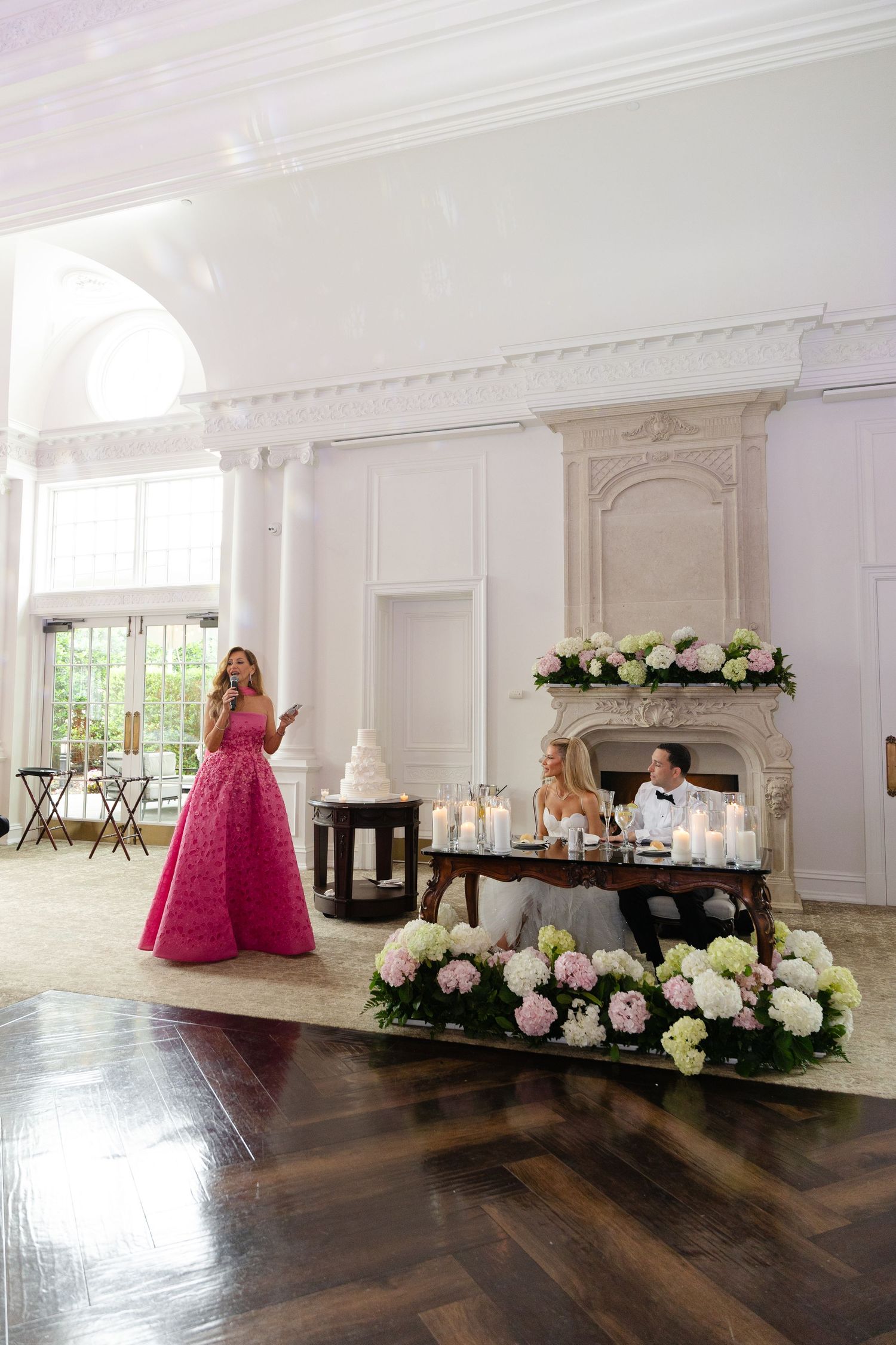 Elegant white ballroom with dark hardwood floors decorated with pink floral arrangements and wedding decor.