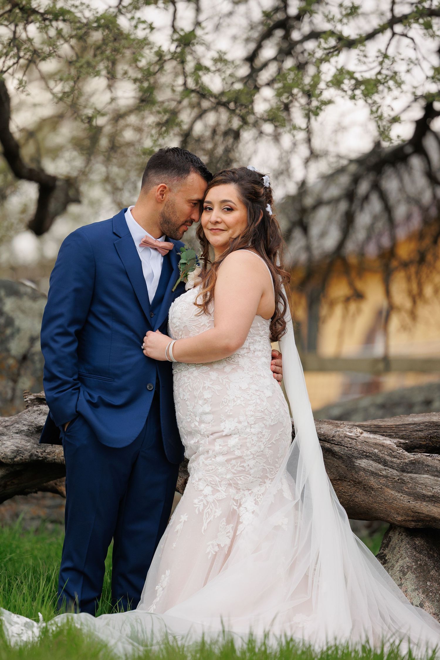 A couple in wedding attire share intimate moments together on a fallen tree trunk in a natural outdoor setting.