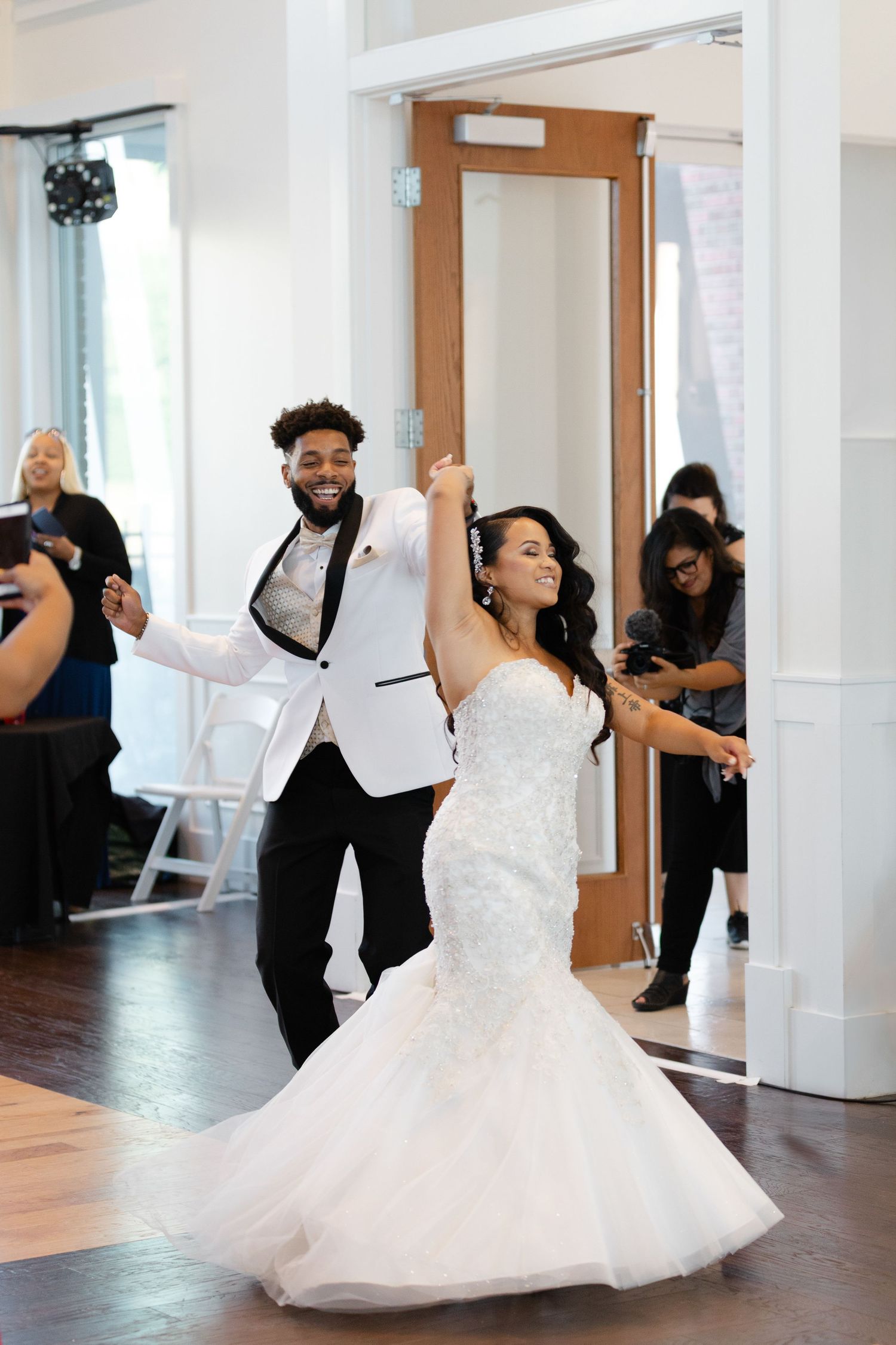 A couple dances together in a bright indoor space, with the bride's white dress twirling gracefully during their choreographed moves.