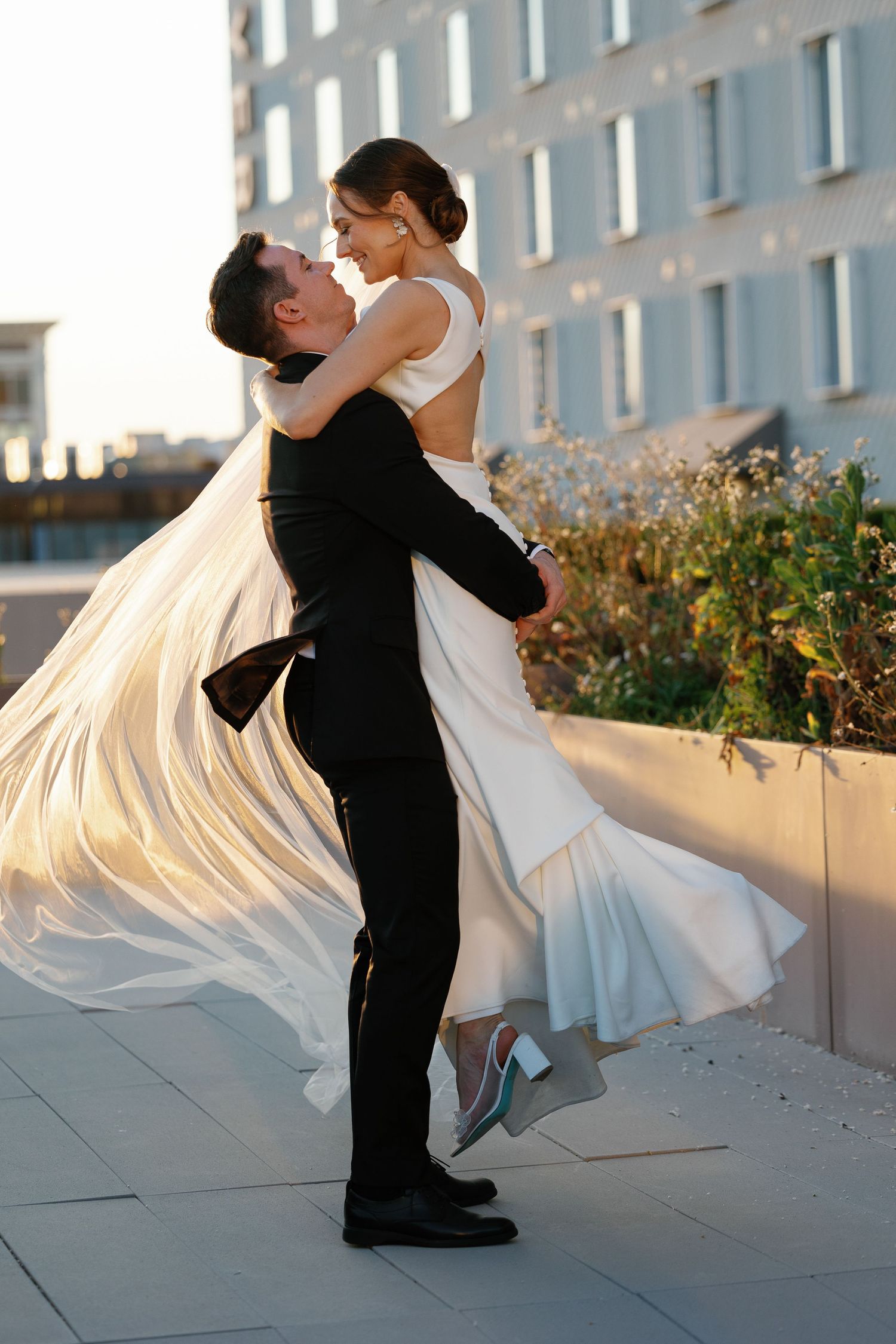 A couple shares an intimate moment on a terrace as the bride's dress flows dramatically in the breeze.