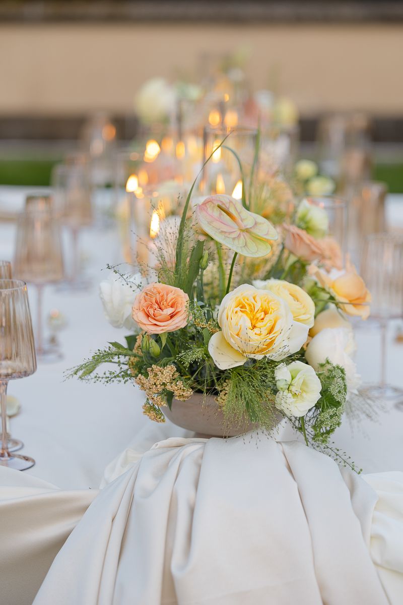 Elegant wedding table centerpieces featuring peach and cream roses with greenery in white linen settings.