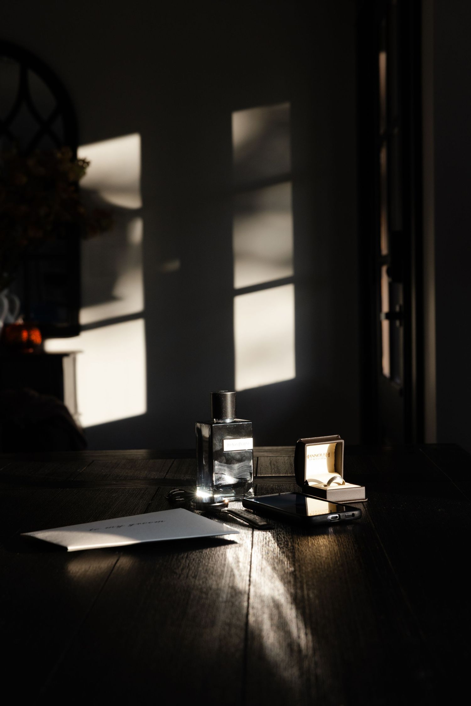 Sunlight casts dramatic shadows across a dark wooden floor with a lantern and papers in moody lighting.
