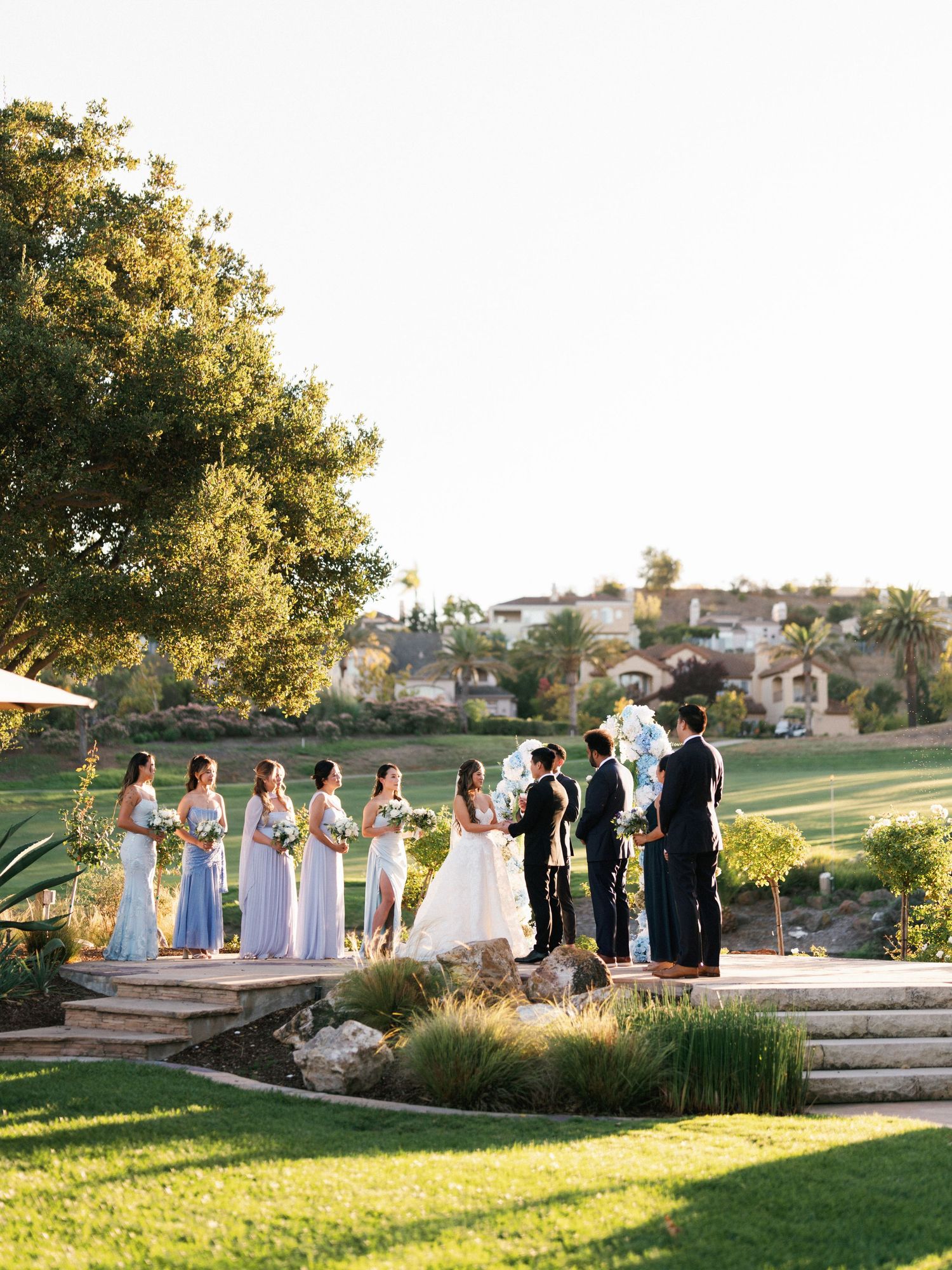 Wedding ceremony at sunset on manicured lawn with bridal party lined up on stone steps.