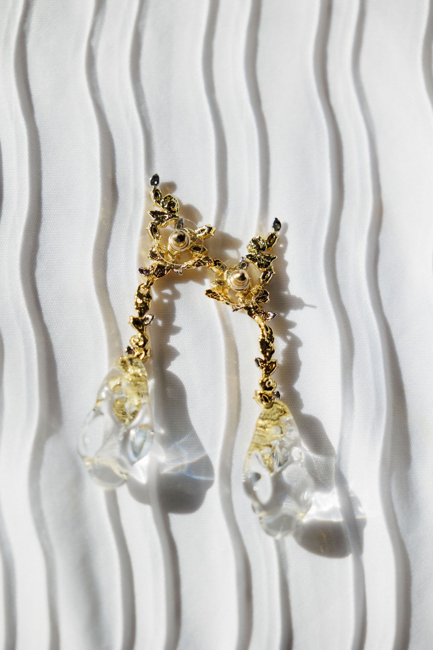 Elegant gold and crystal drop earrings photographed on a white textured background with wavy lines.