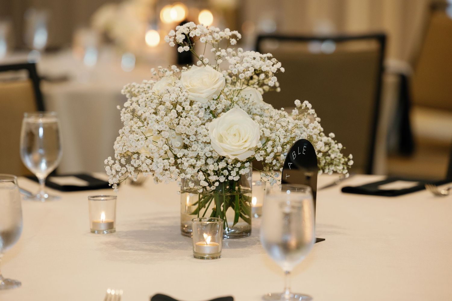 Elegant wedding centerpiece with white roses and baby's breath in a mason jar on a formal dining table.
