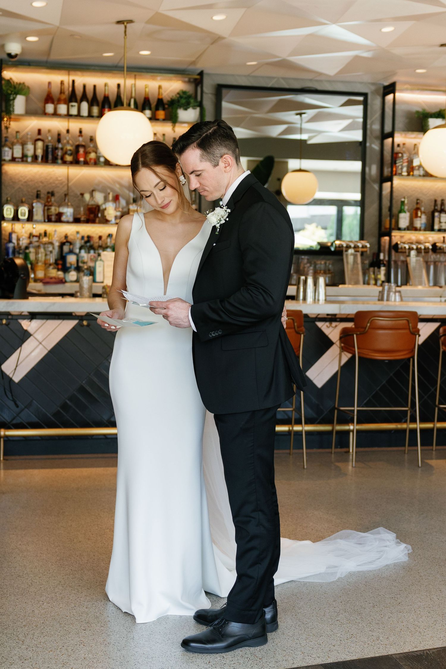 A couple in wedding attire share an intimate dance moment in a modern restaurant bar setting with soft lighting.