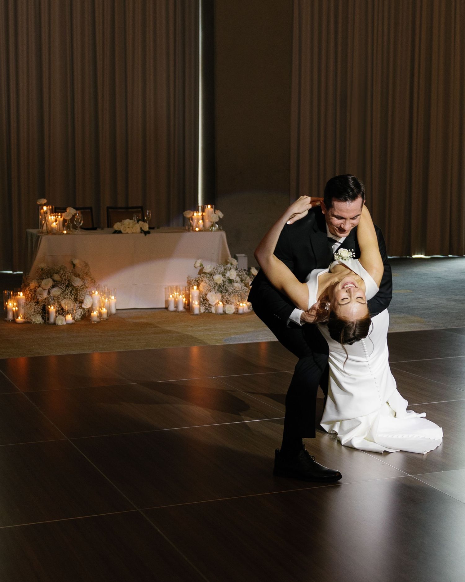 A romantic dance dip between two people in formal attire during a wedding reception with candlelit decor in the background.