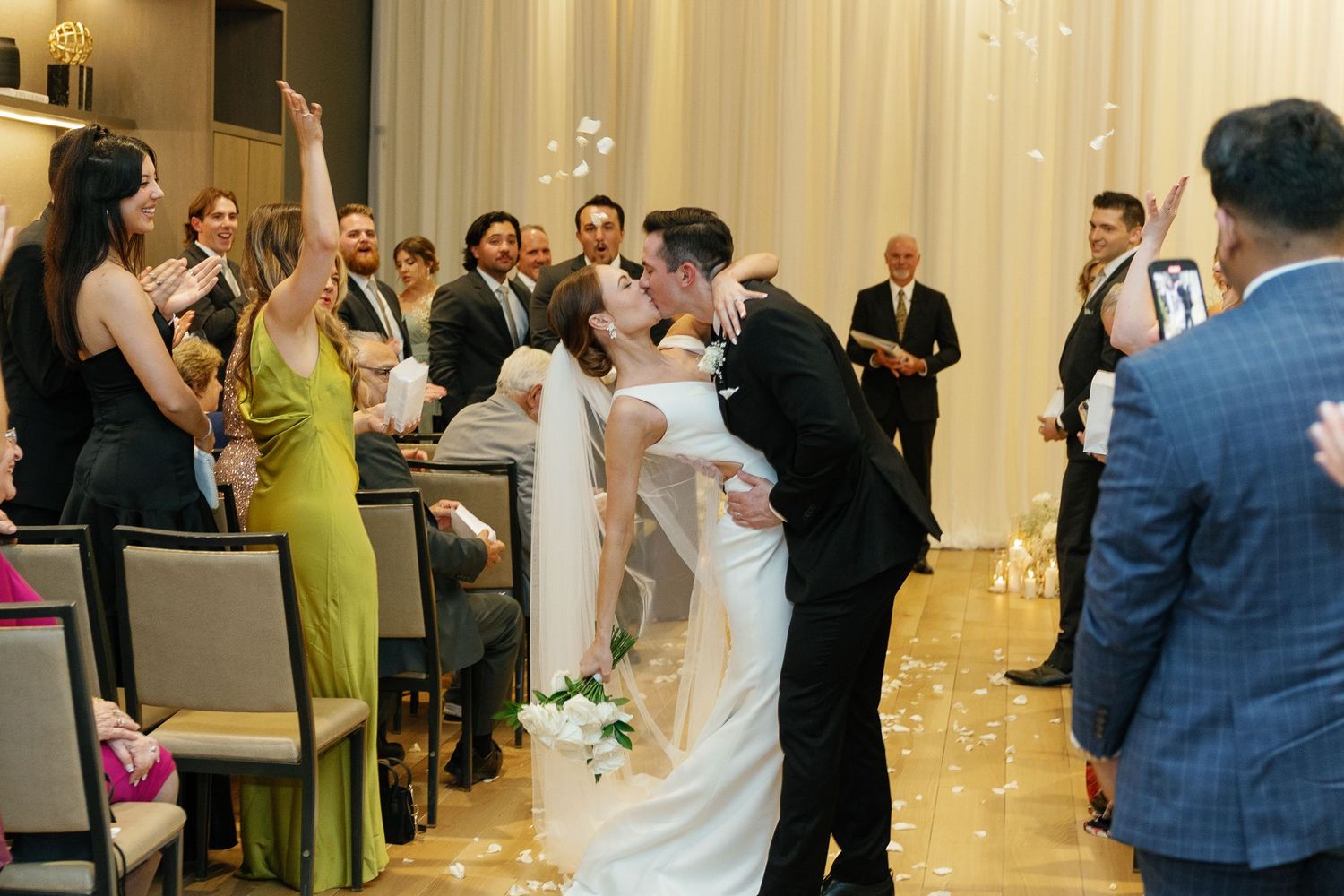 Wedding guests dance and celebrate together on the dance floor at an elegant reception venue with white curtains.