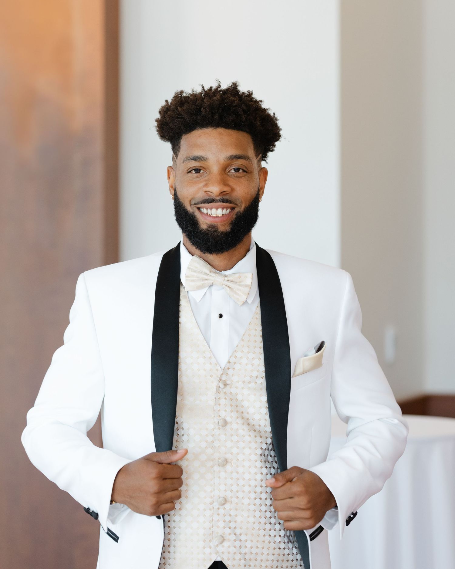 A person wearing a white tuxedo jacket with black lapels and polka dot vest poses in a formal setting.
