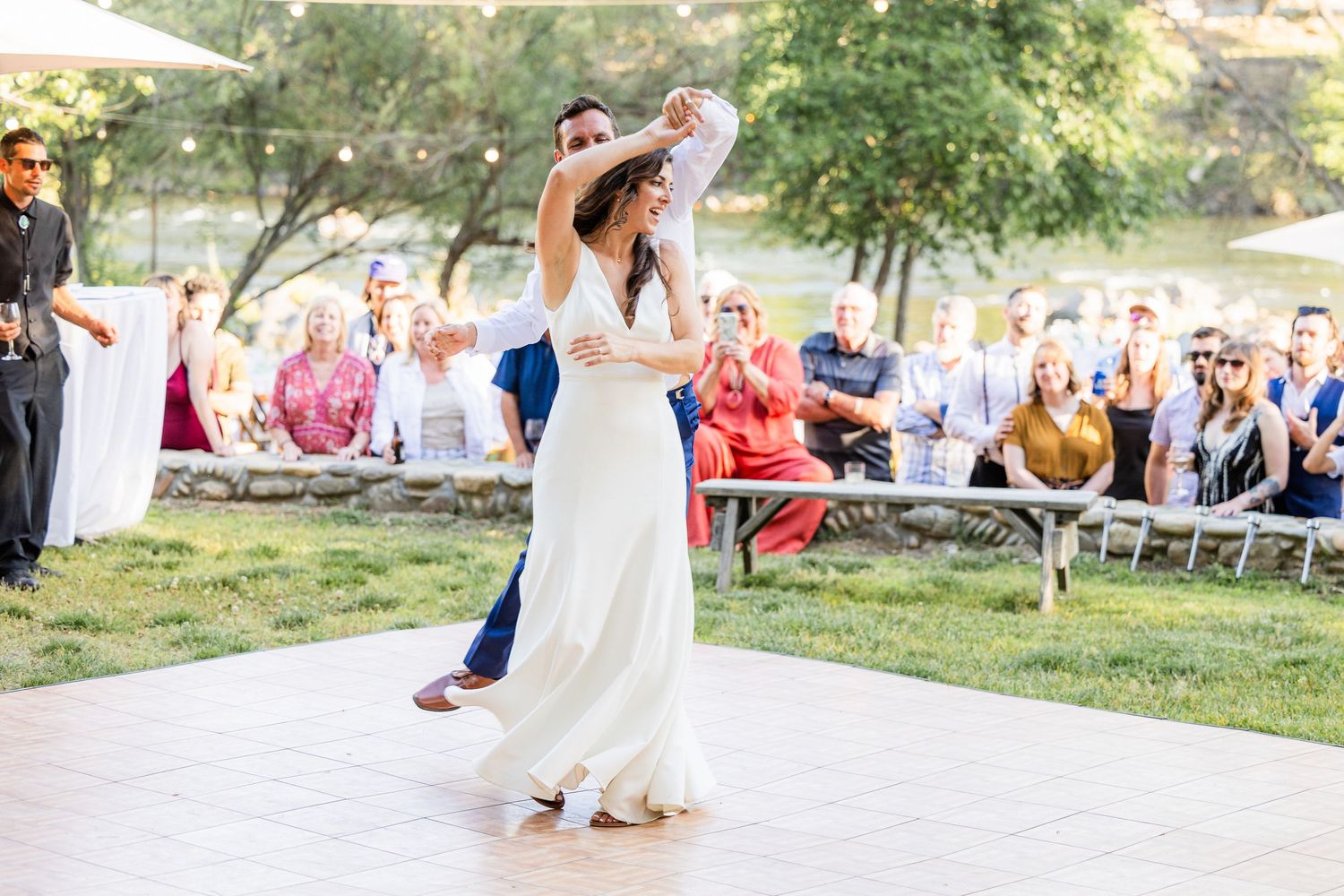 Couple performs elegant first dance outdoors at sunset wedding reception with guests watching from lawn seating.