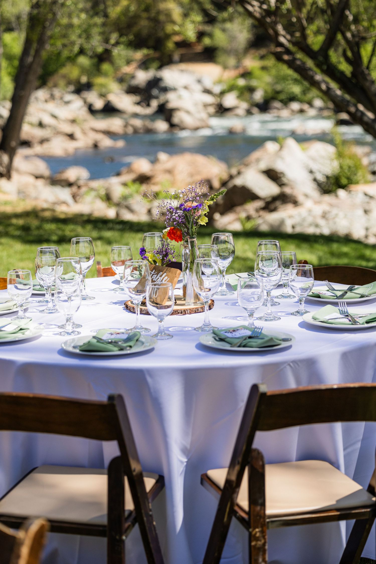 Elegant outdoor table settings with white tablecloths, wine glasses and place settings arranged for a garden event.