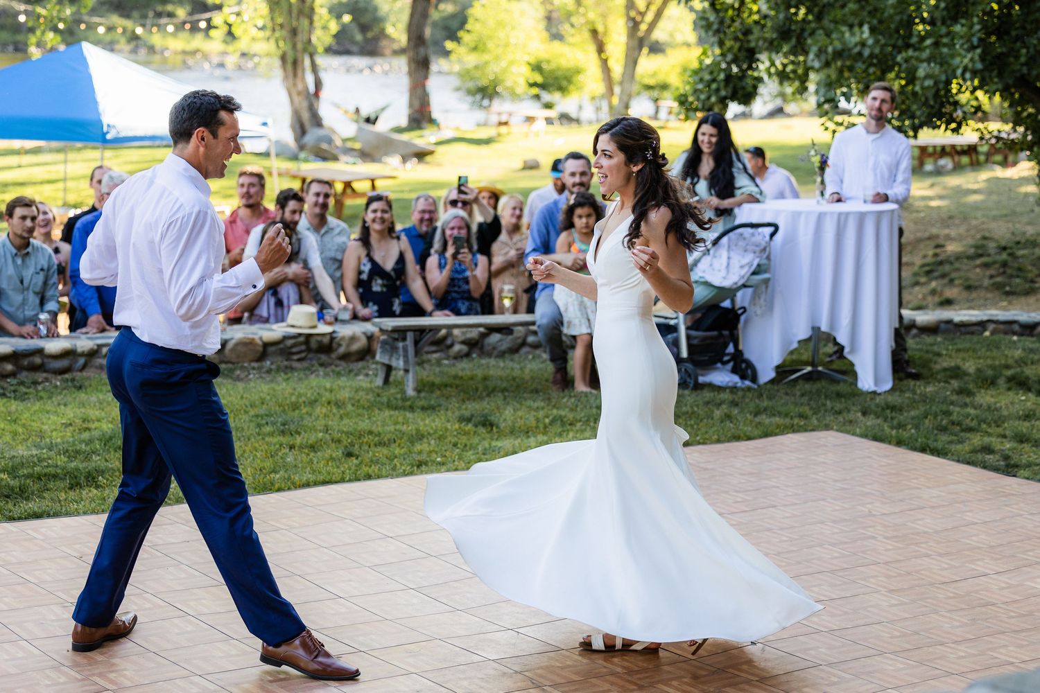 A couple performs a choreographed dance routine on an outdoor dance floor at a sunny wedding reception.