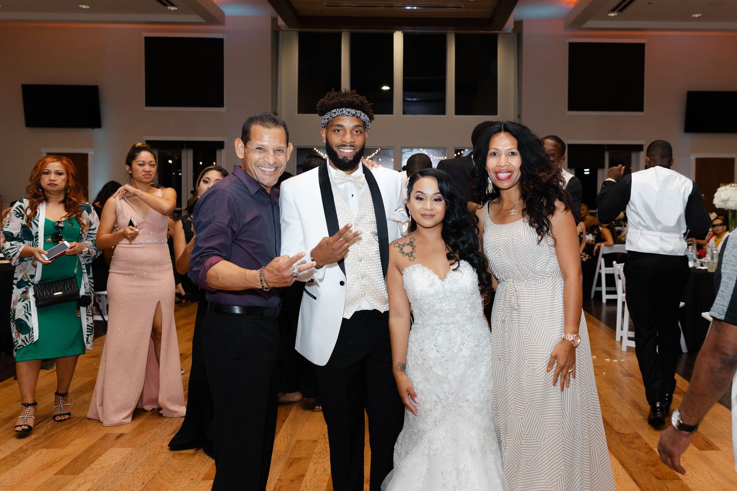 Wedding guests dance and celebrate on a wooden dance floor during an indoor reception celebration.