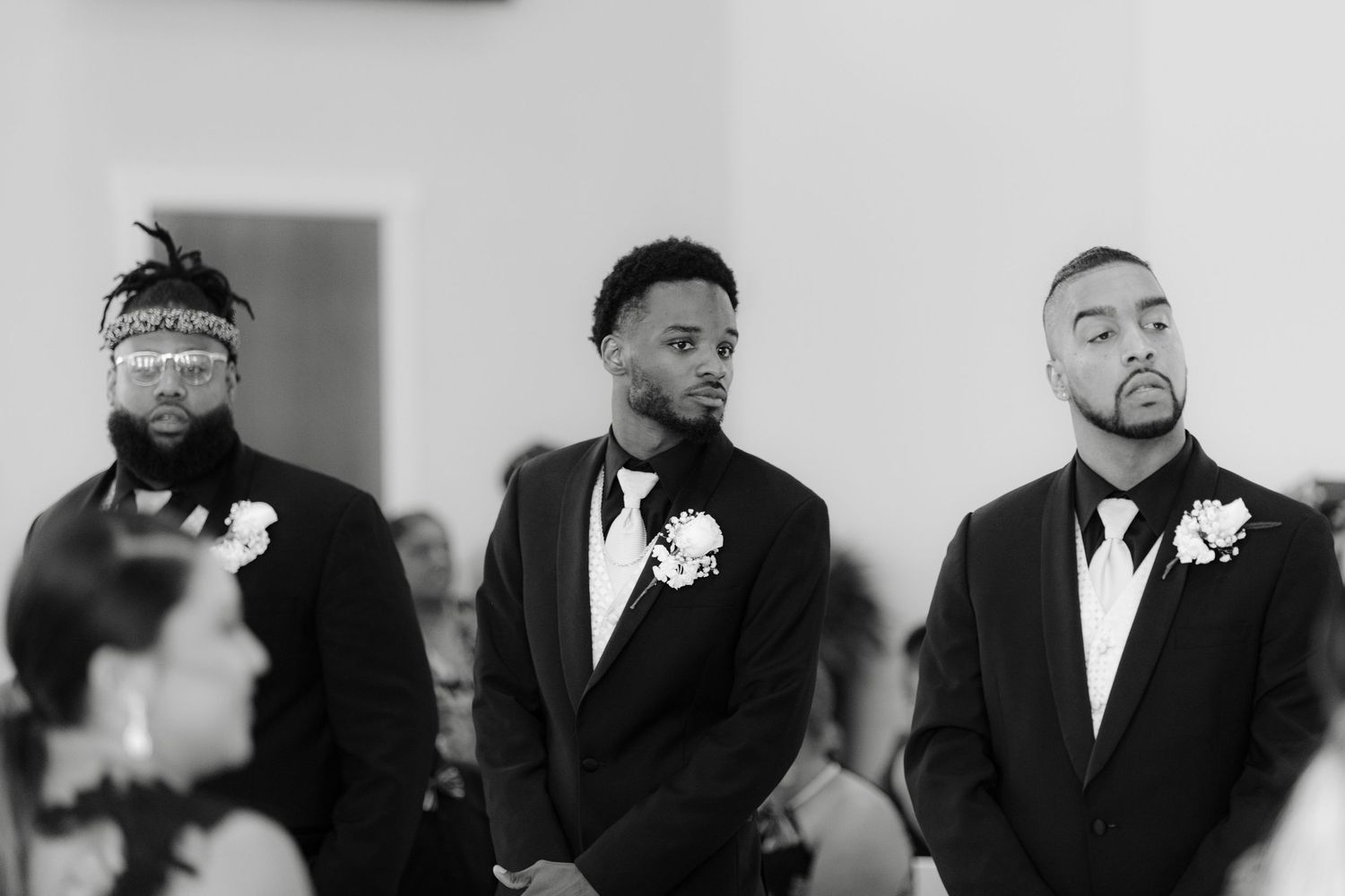 A black and white panoramic photo showing groomsmen in formal tuxedos lined up at a wedding celebration.