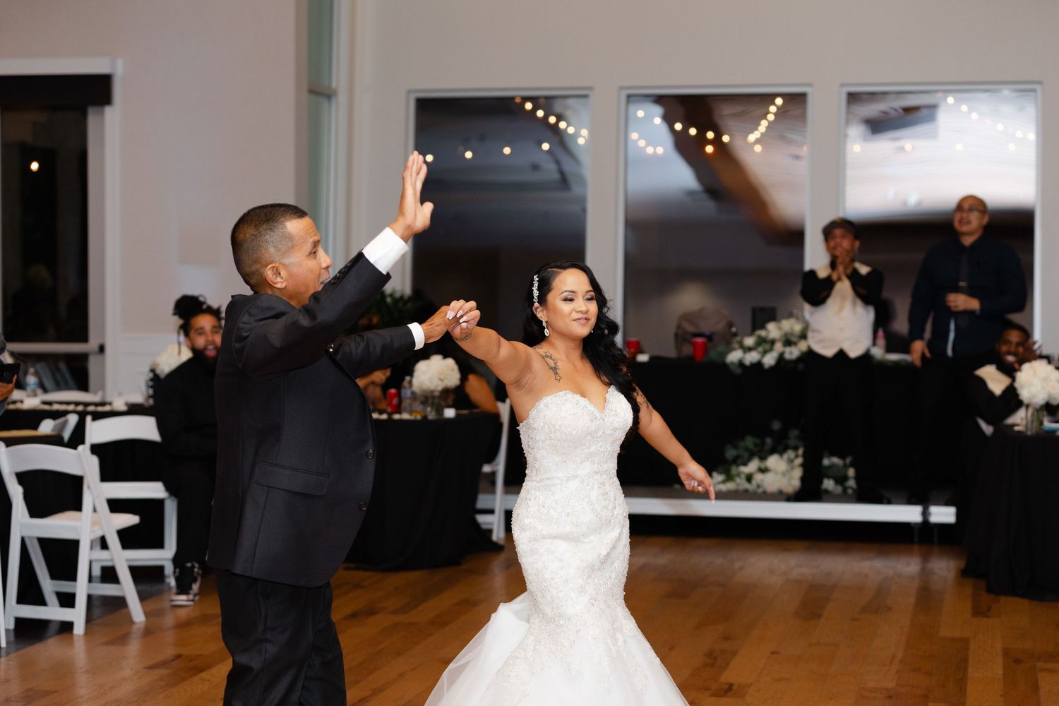 A couple dances together during their wedding reception in a spacious ballroom with white chairs and decor.