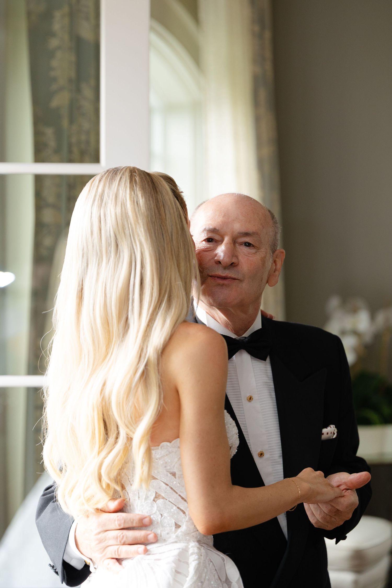 Two people in formal attire share a tender moment during what appears to be an elegant event.