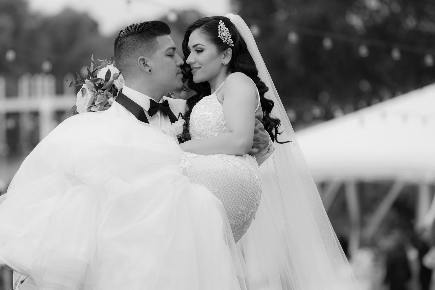 A romantic black and white wedding photo showing a tender moment between newlyweds in elegant wedding attire.