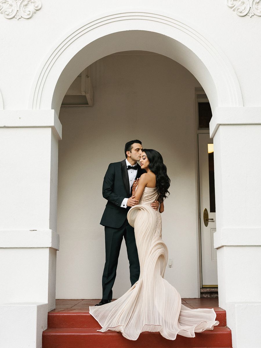 A couple shares a romantic moment in an elegant white archway during their wedding photoshoot.