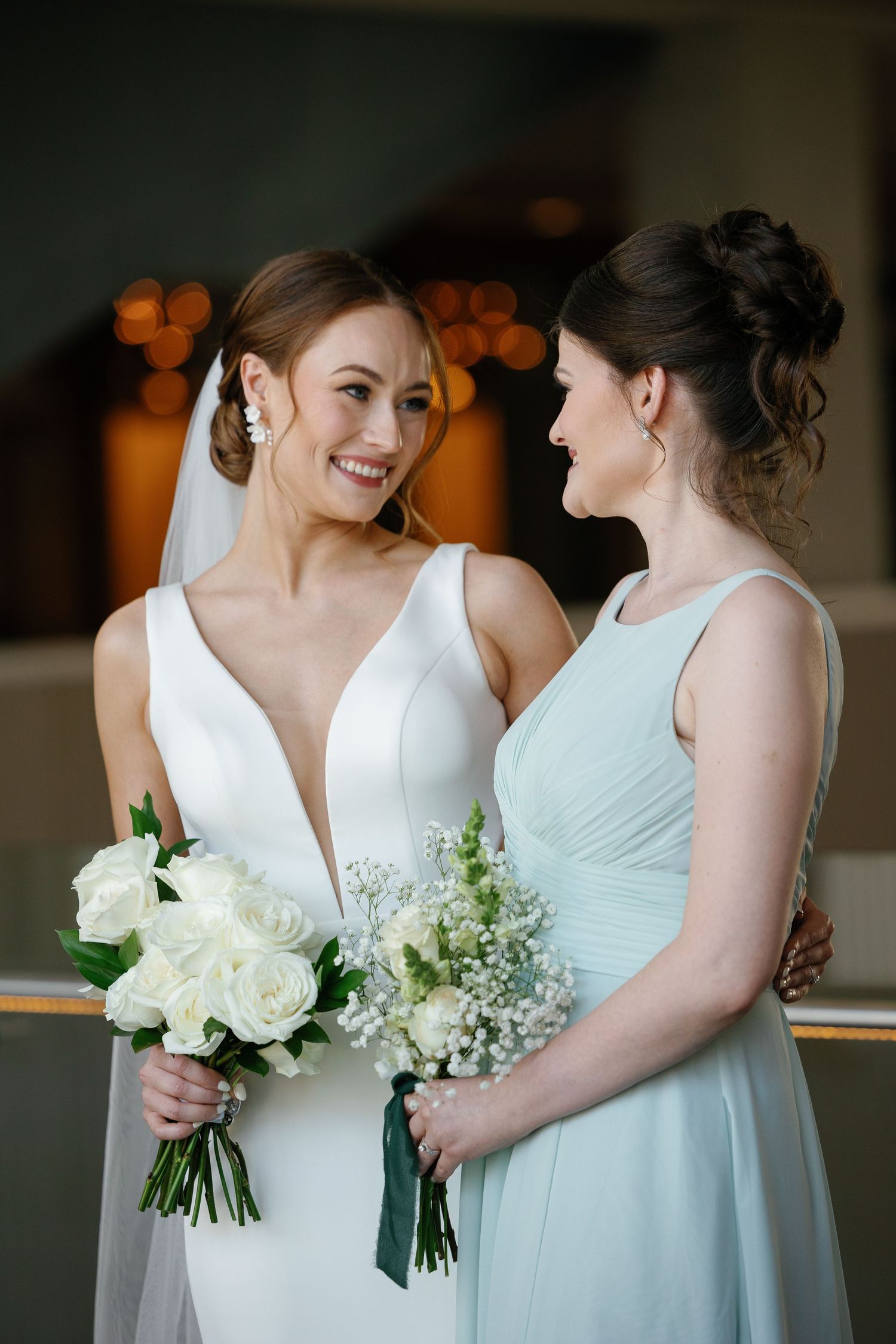 Two people in wedding attire share a candid moment while holding white floral bouquets.