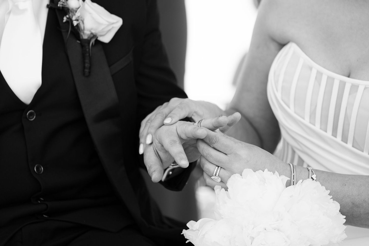 A black and white wedding photo showing clasped hands and a white bridal gown with a bouquet.