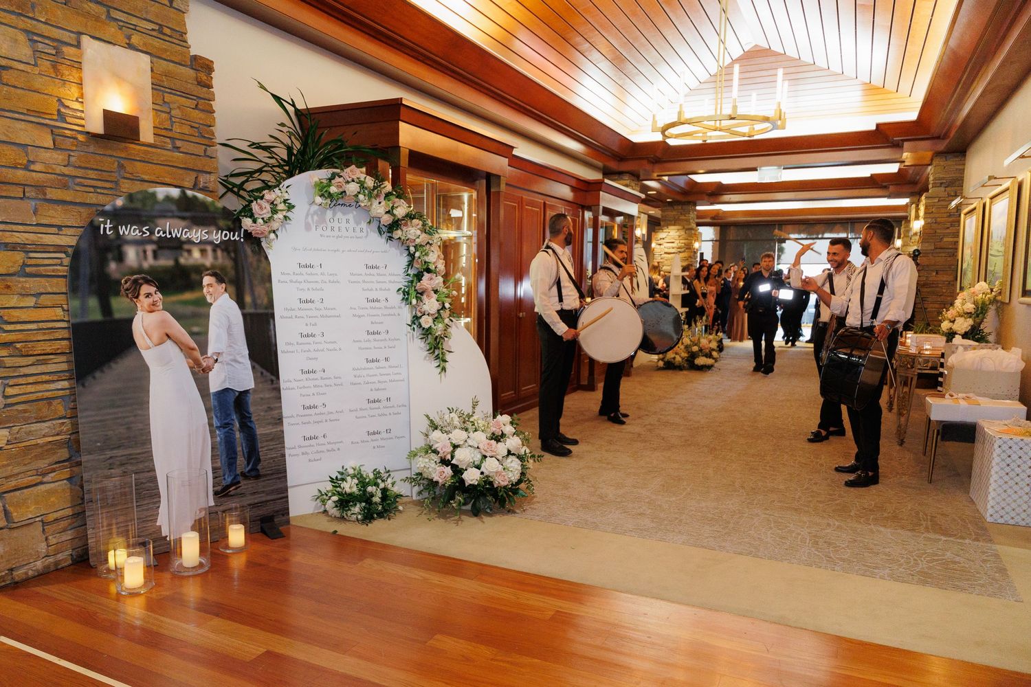 Wedding guests gather in an elegant wood-paneled reception hall with stone walls and warm lighting.