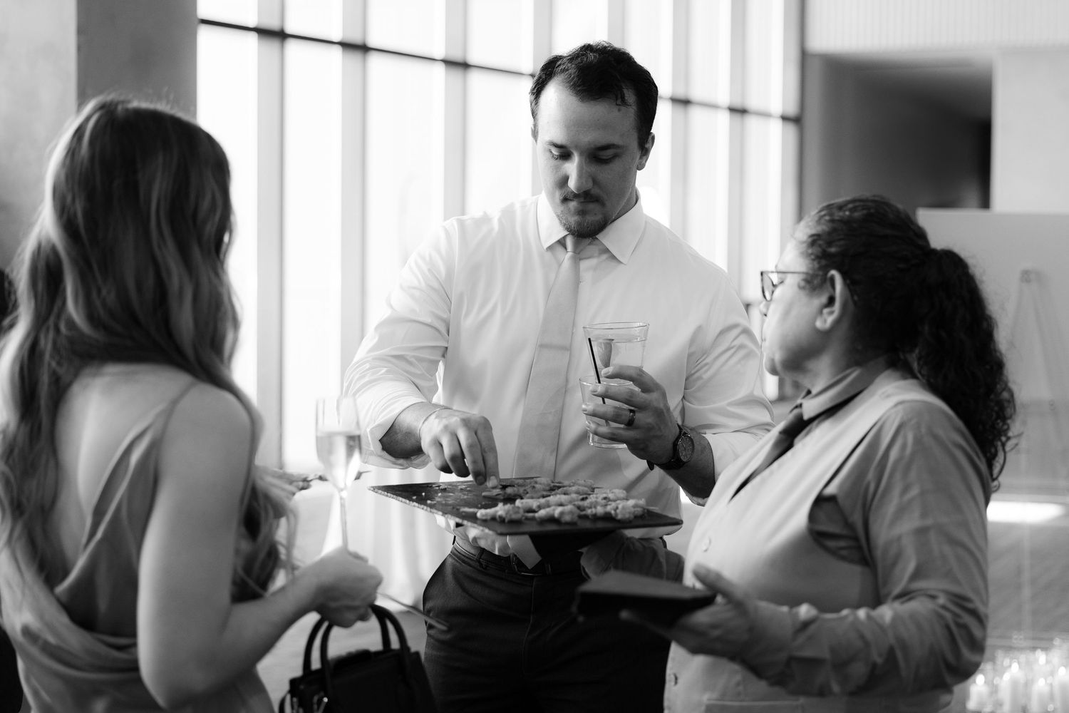 A server in a white shirt takes orders from customers at a restaurant table in black and white photography.