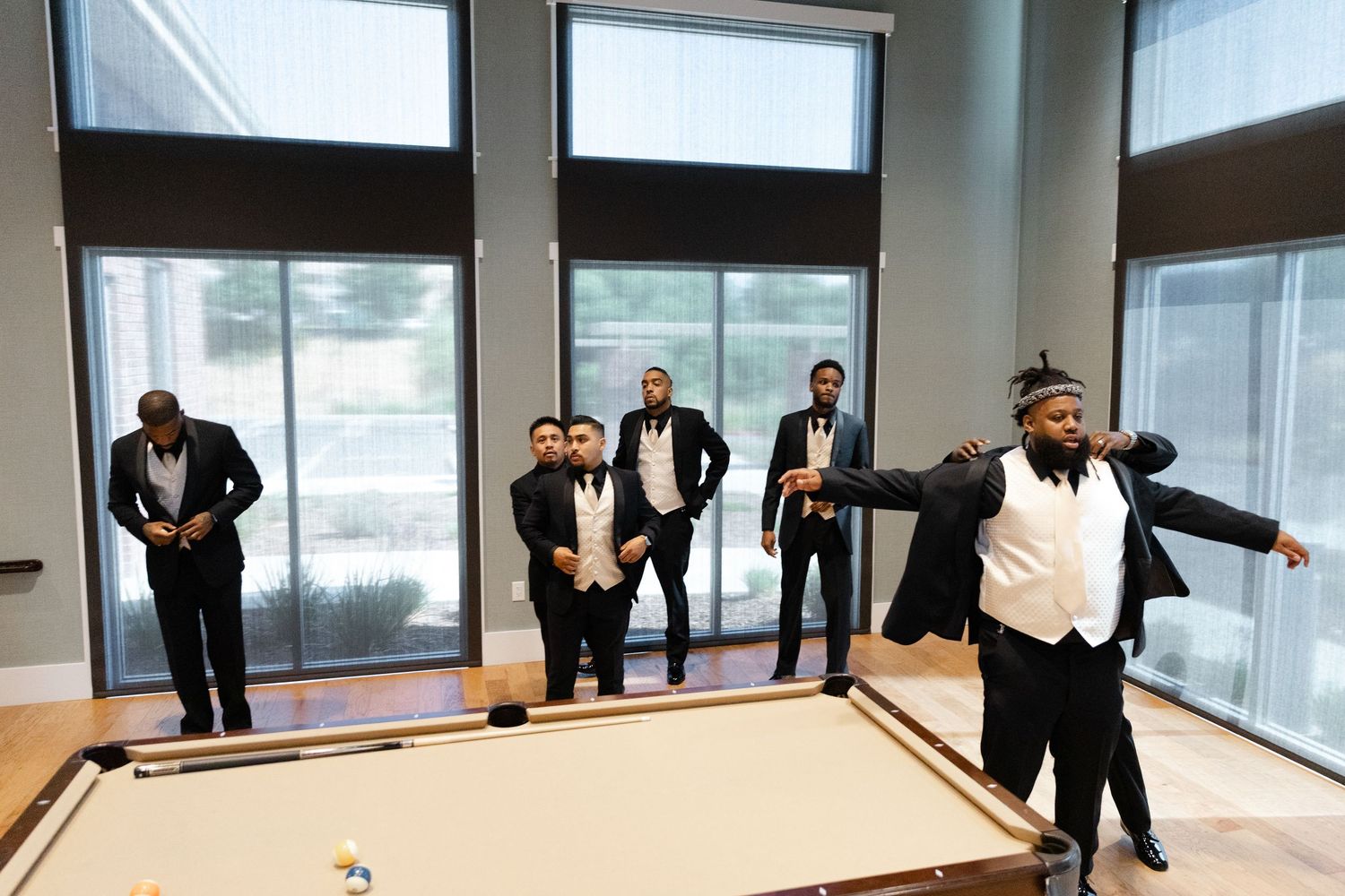 Groomsmen having fun playing pool in formal attire during wedding preparations.