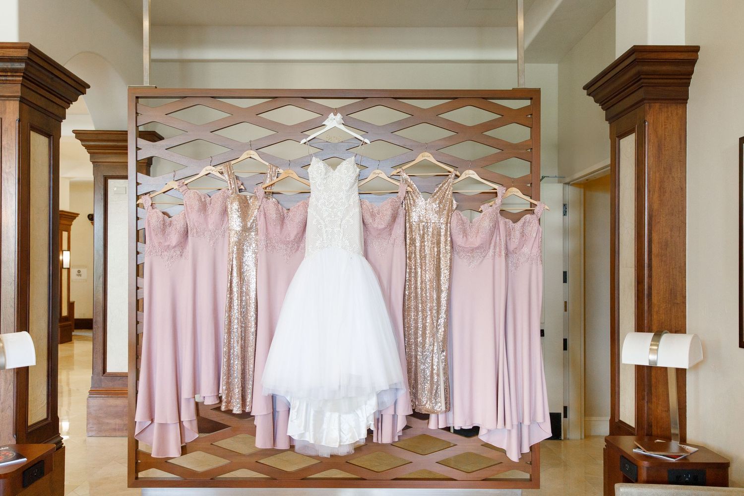Row of blush pink and white bridesmaid dresses and wedding gowns hanging on display in an elegant dressing room.