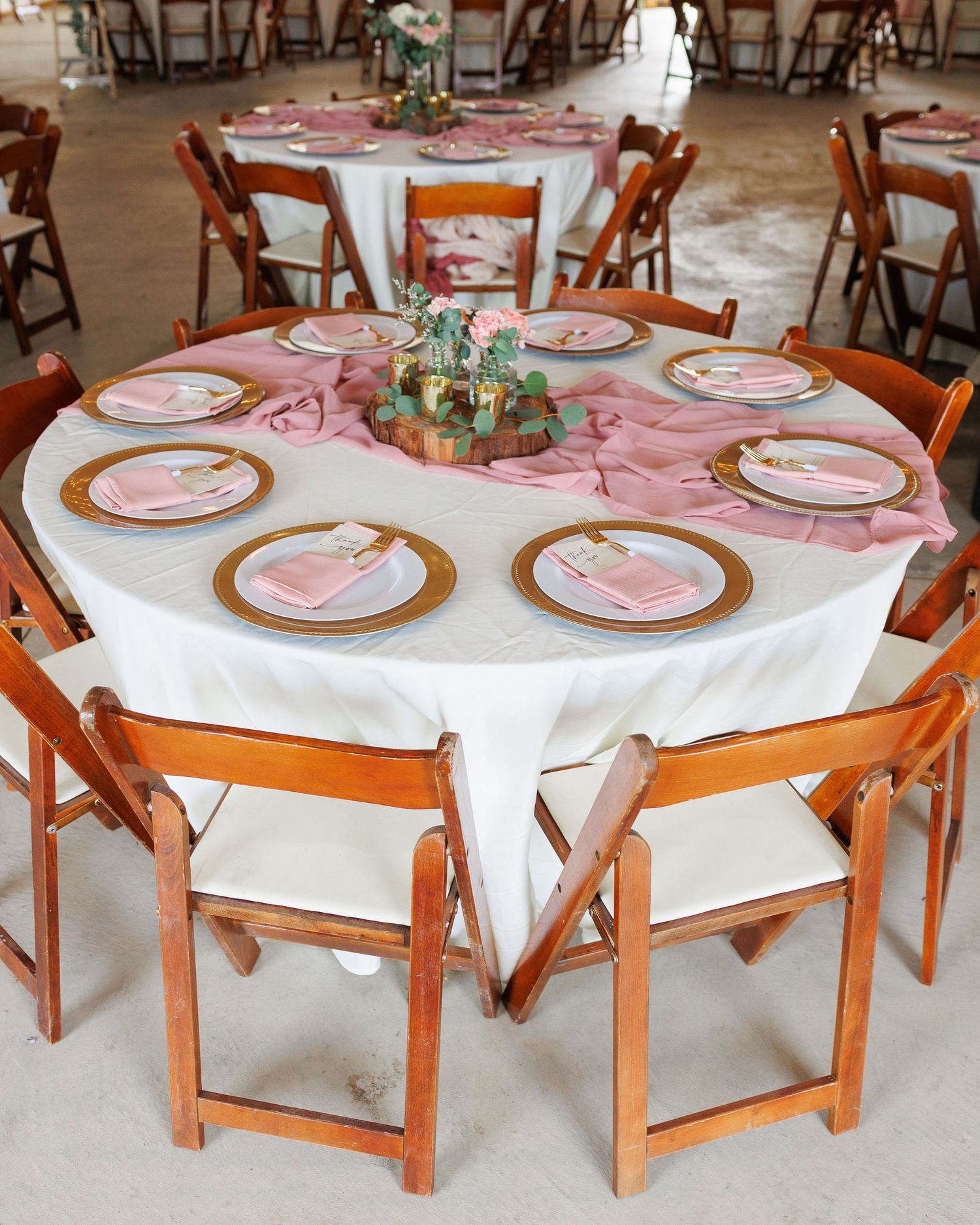 Round tables with white tablecloths, pink napkins, and wooden chairs set up for a formal dining event.