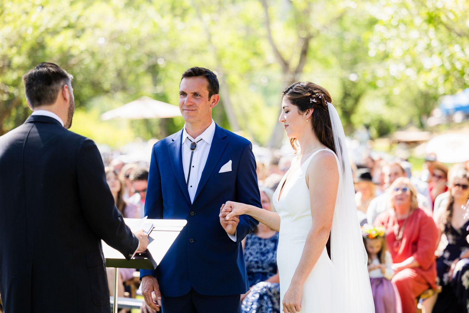 A joyful outdoor wedding ceremony with guests gathered in a sunny garden setting.
