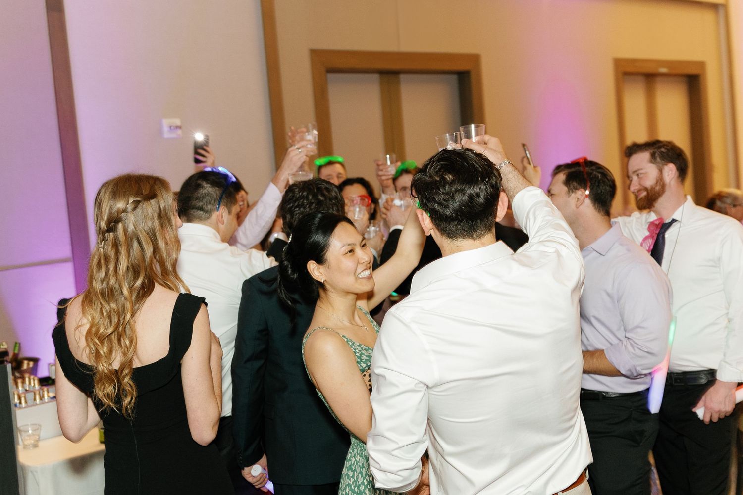 People dancing and celebrating at a wedding reception with purple lighting and a festive atmosphere.