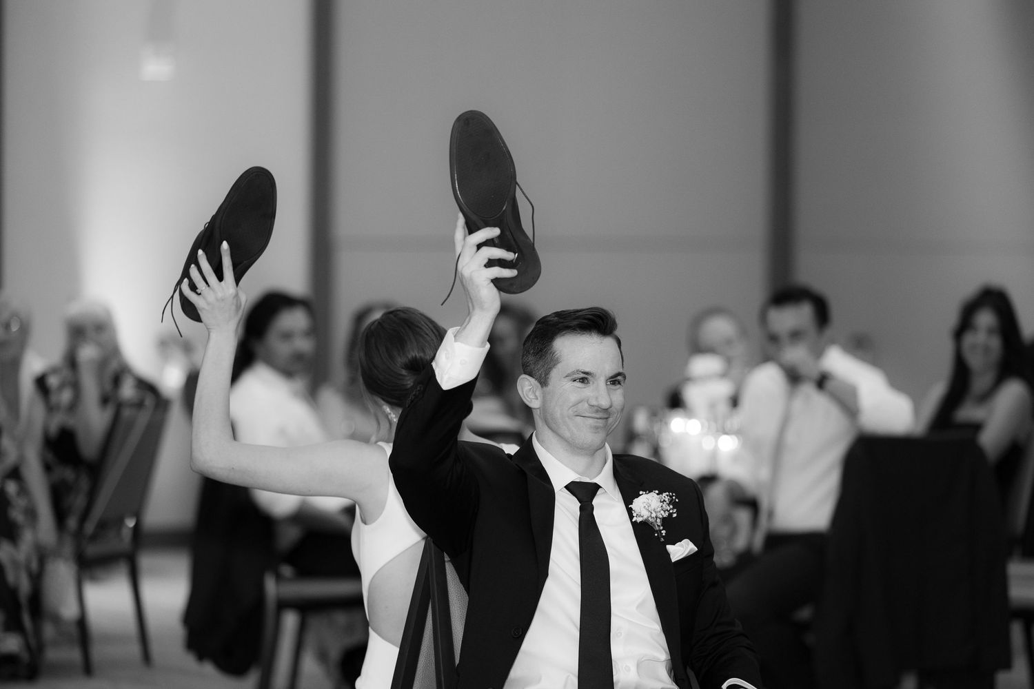 A black and white photo captures a couple's first dance at their wedding reception with guests watching.