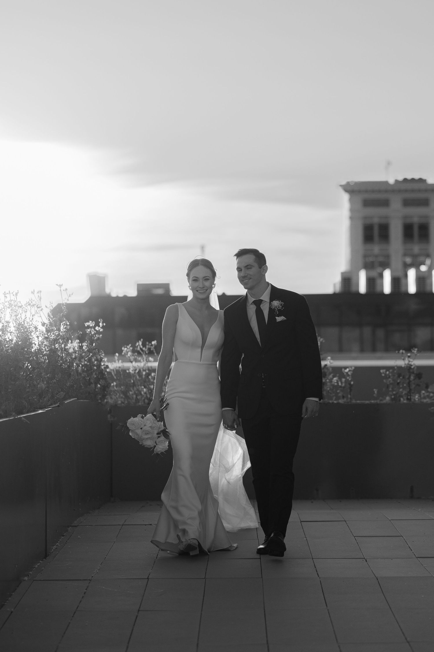 A black and white wedding photo of a couple on a rooftop terrace with city buildings in the background.