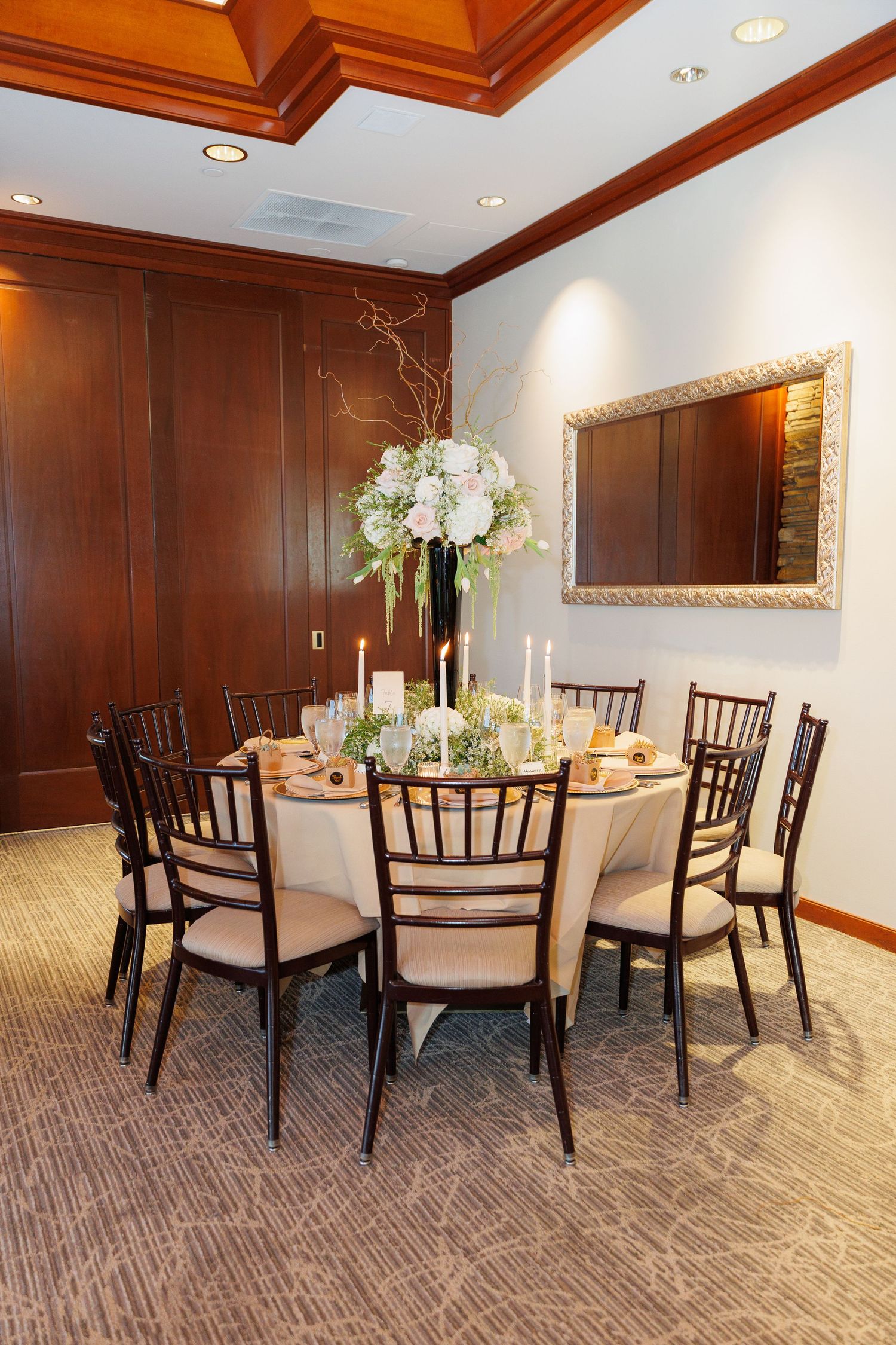 Elegant dining room with wooden coffered ceiling, dark chiavari chairs, and white tablecloths in a banquet setting.