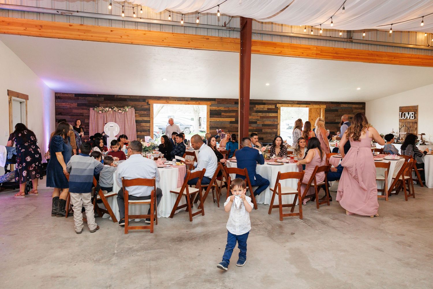 People sit in wooden chairs arranged in rows during an indoor event in a white-walled room.