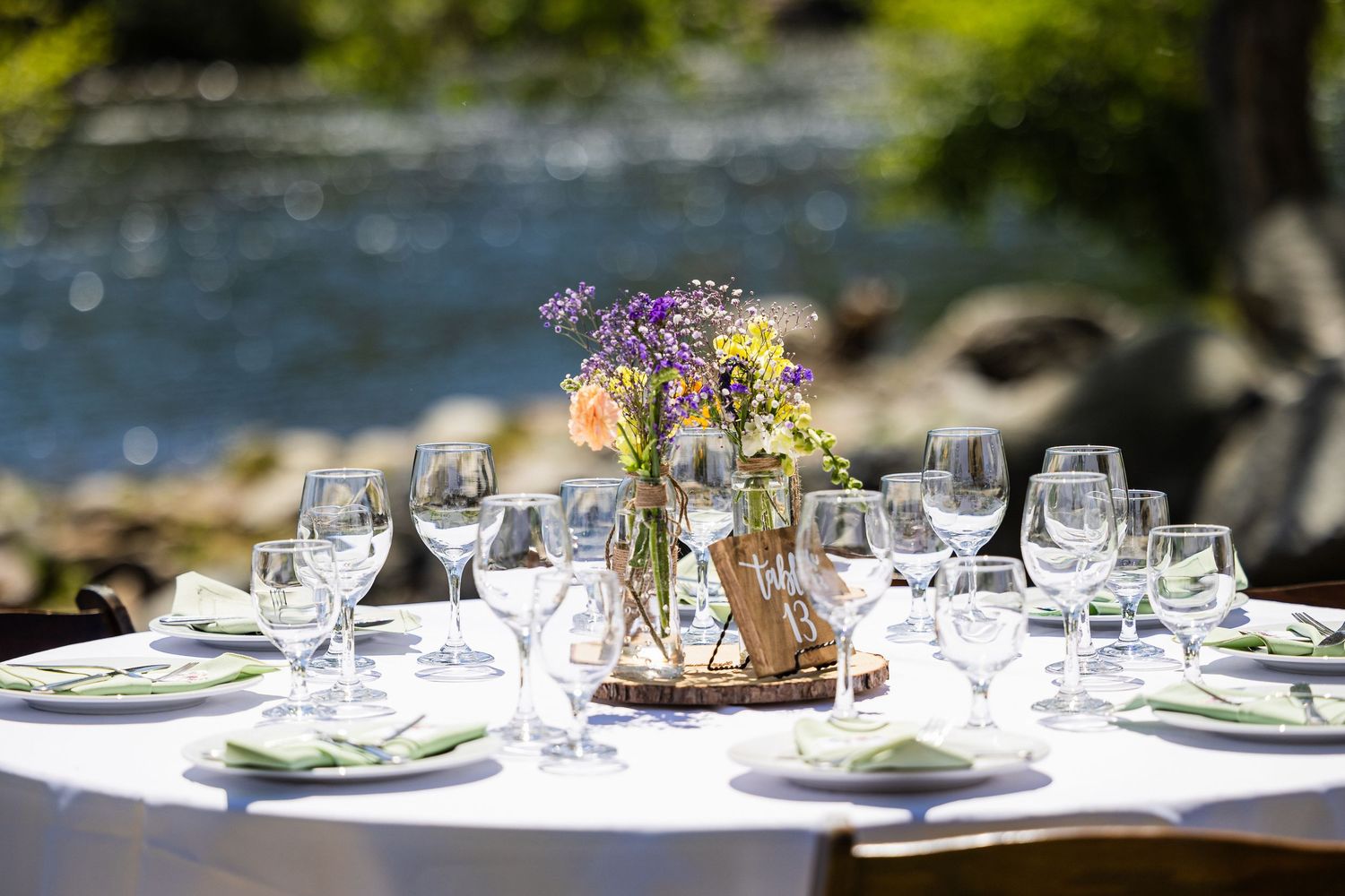 Elegant outdoor table settings with white linens, wine glasses, and floral centerpieces at a garden event.