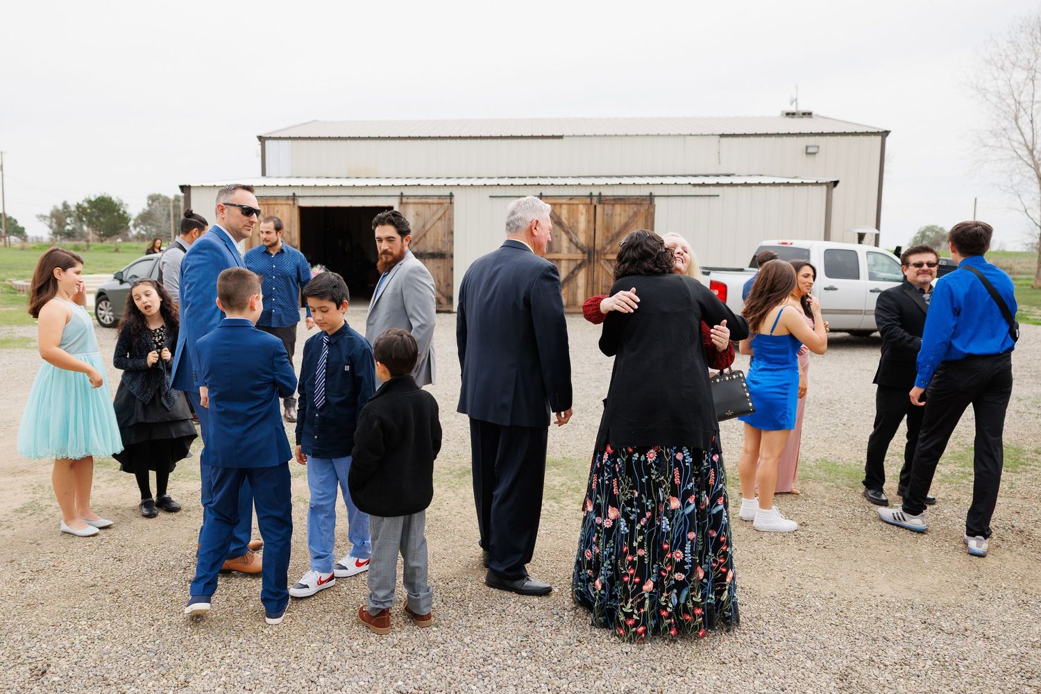 A group of people gather outside a rustic barn building during a casual outdoor event.