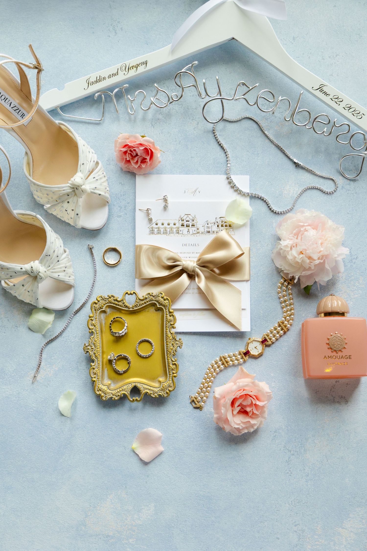 Elegant wedding accessories including rings, bows, flowers, and delicate decorative items arranged on a light blue background.