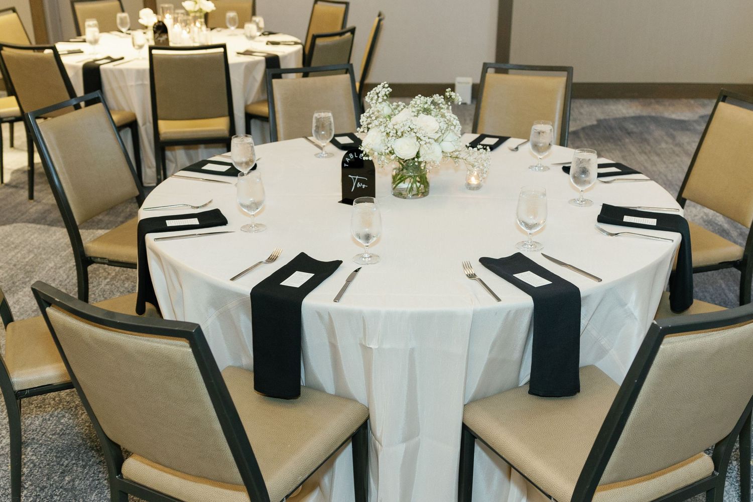 Elegant round dining table with white tablecloth, navy napkins, and simple floral centerpiece at formal event setting.