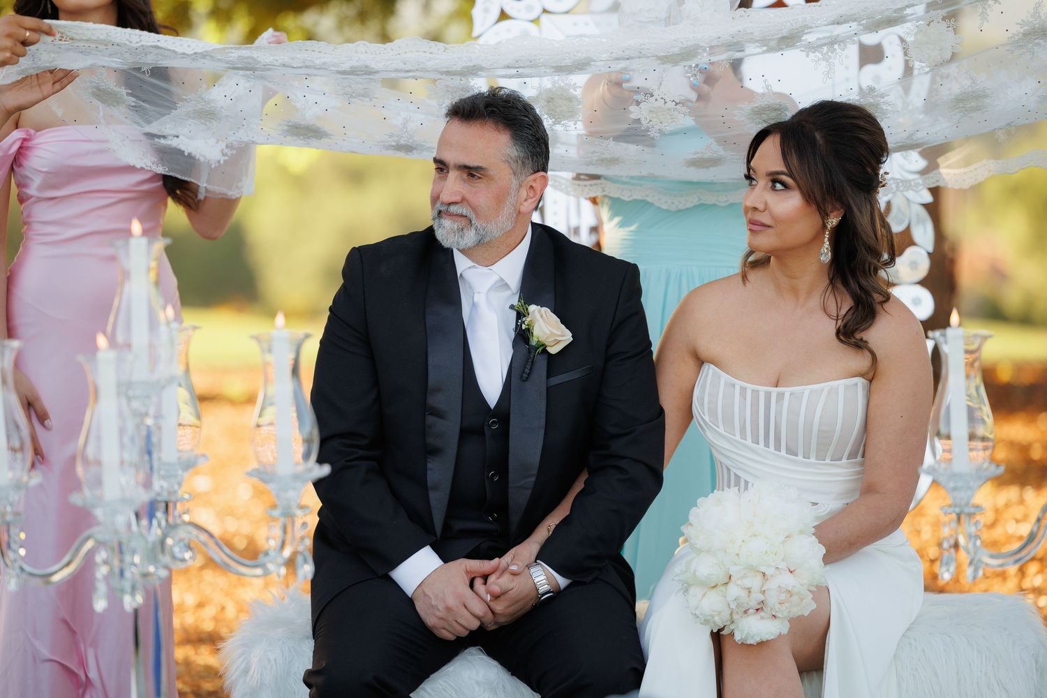A bride and groom share a candid moment during their outdoor wedding ceremony at sunset.