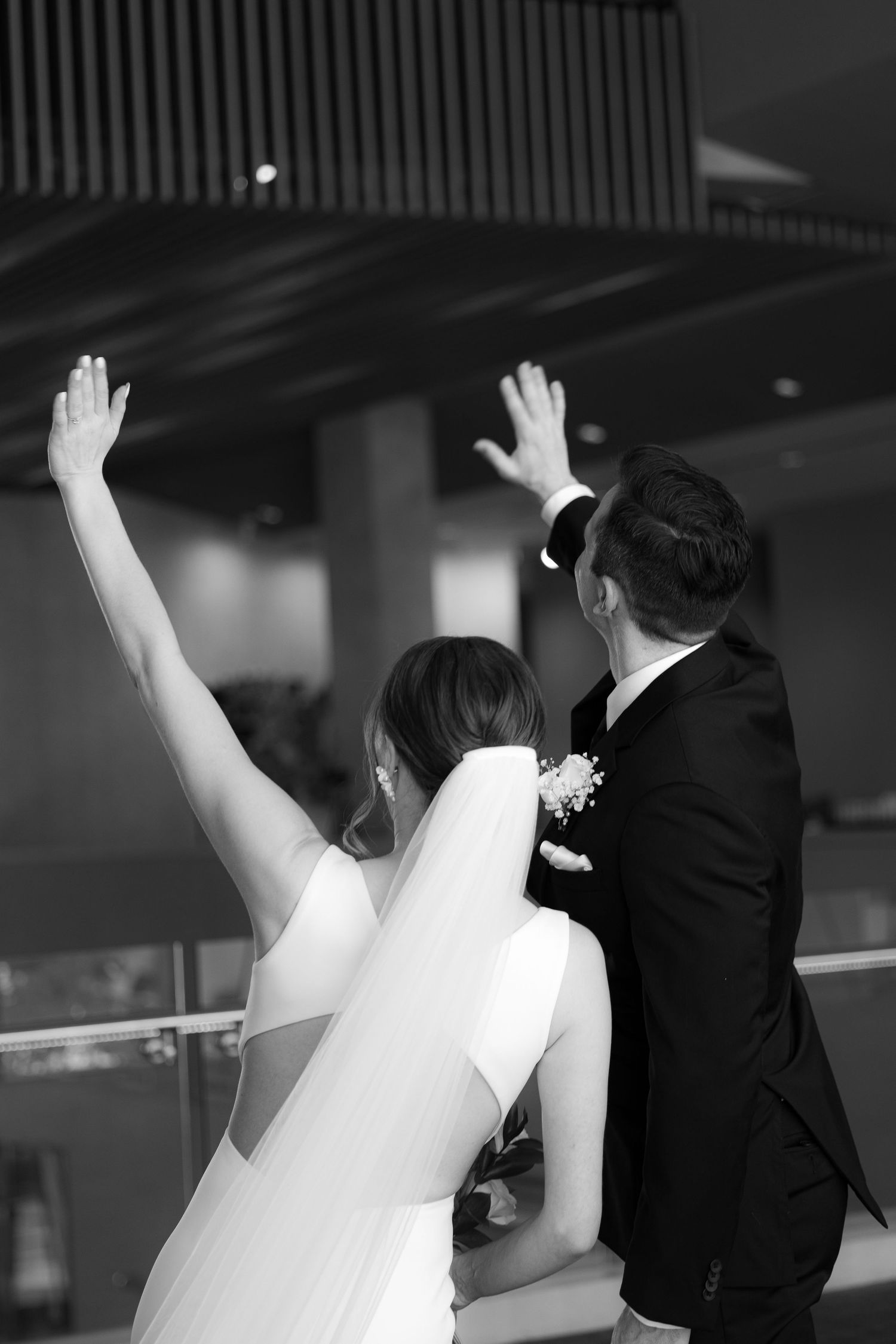 A bride and groom raise their hands in celebration at their wedding reception, captured in black and white.