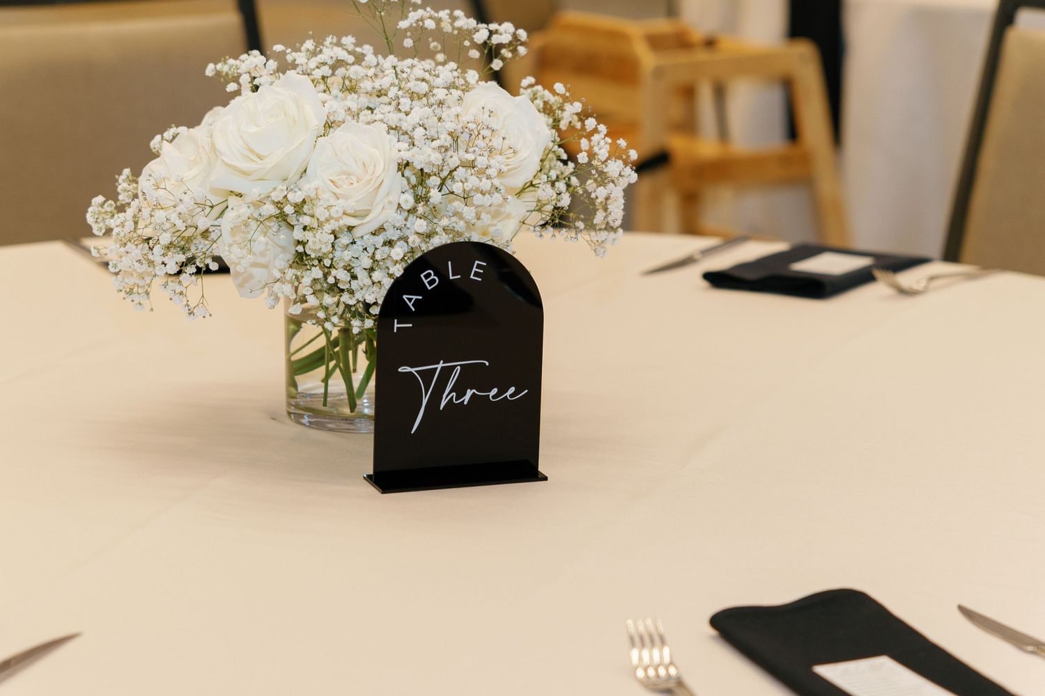 Elegant table setting with baby's breath flowers, black place cards, and white linens for a modern wedding reception.