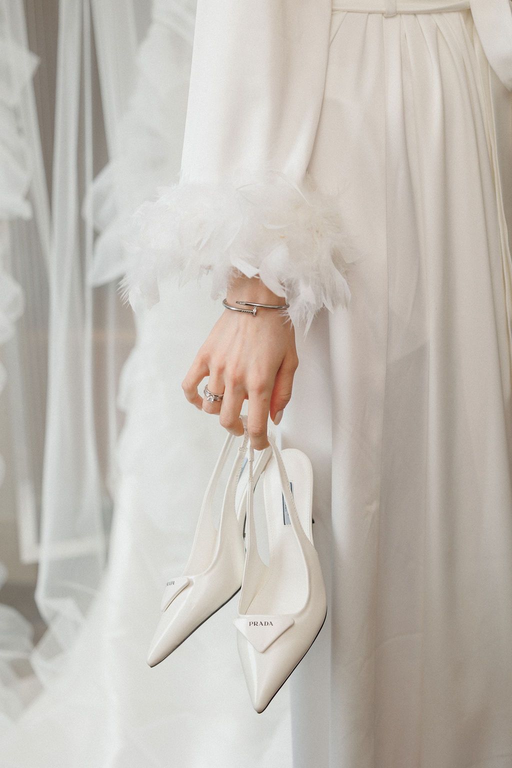 Close-up shots of hands holding elegant white bridal heels against a white dress background.