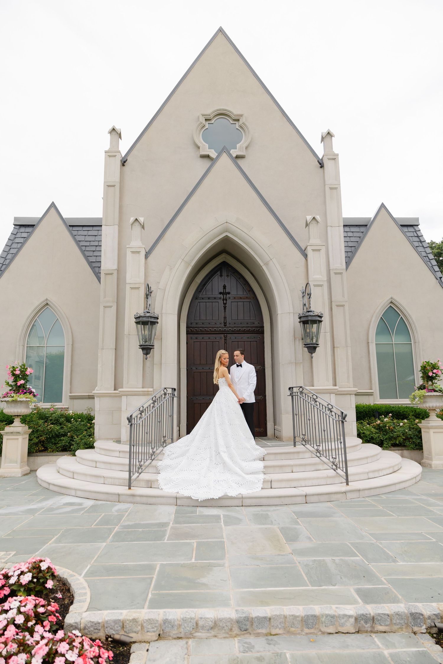 A wedding couple stands on the steps of a Gothic-style church with cream colored walls and arched doorways.