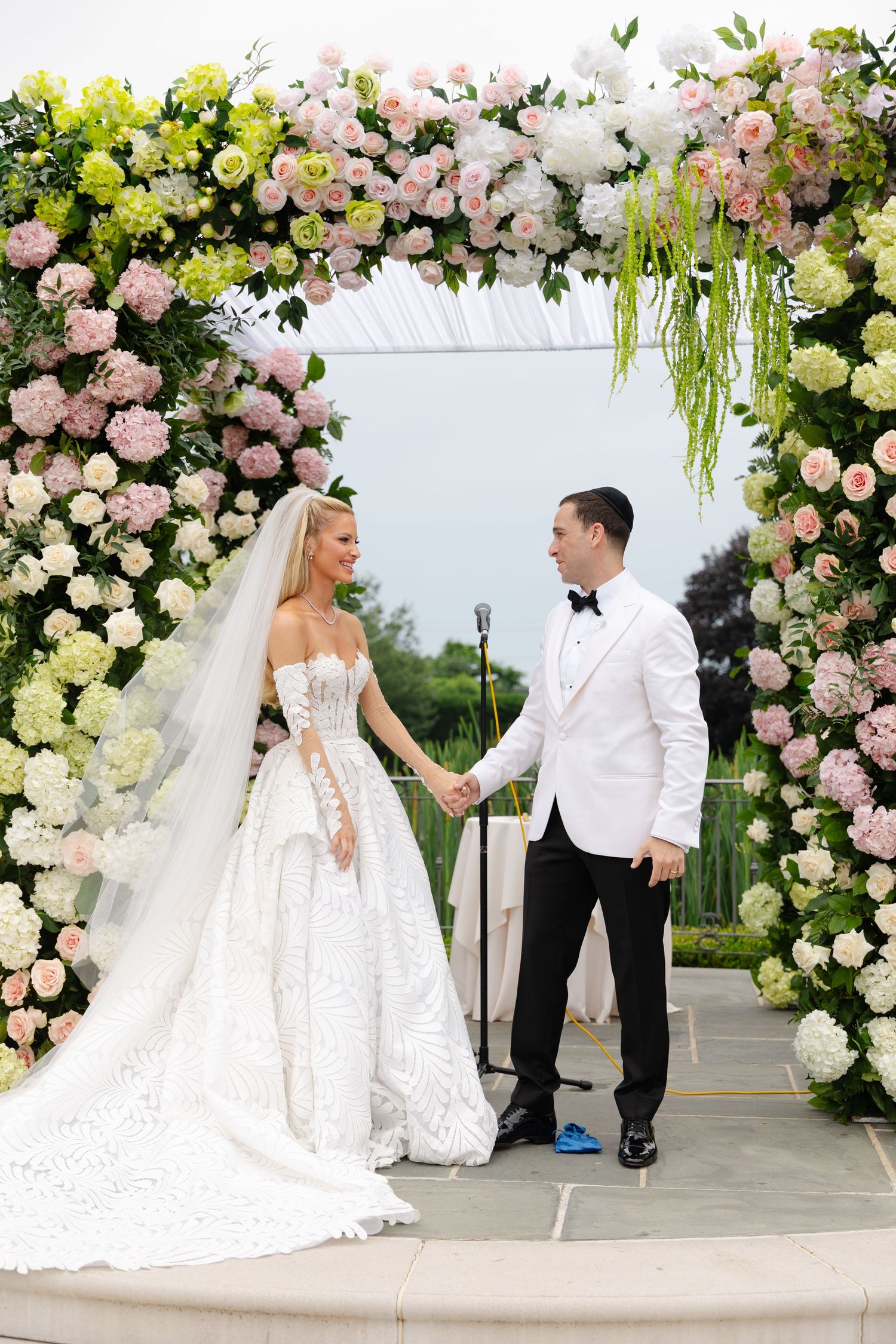 A wedding ceremony setup with a stunning floral arch featuring pink and white roses with cascading greenery.
