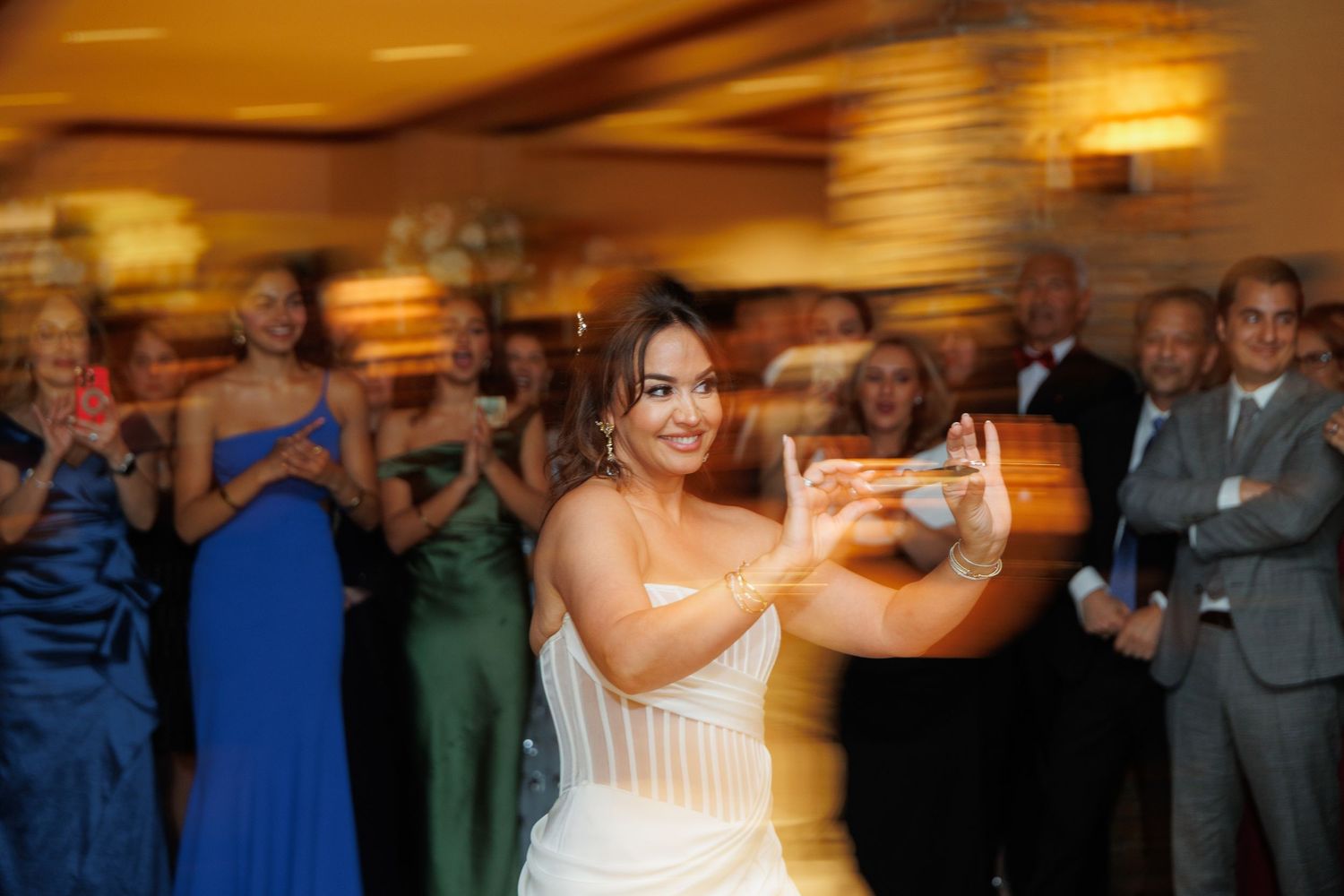 A person in a white wedding dress dances with arms outstretched while guests watch in the background.
