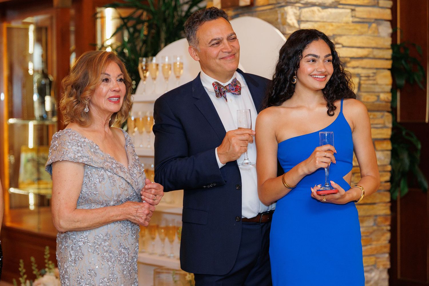People in formal attire laughing and enjoying themselves at an elegant indoor venue with stone walls.