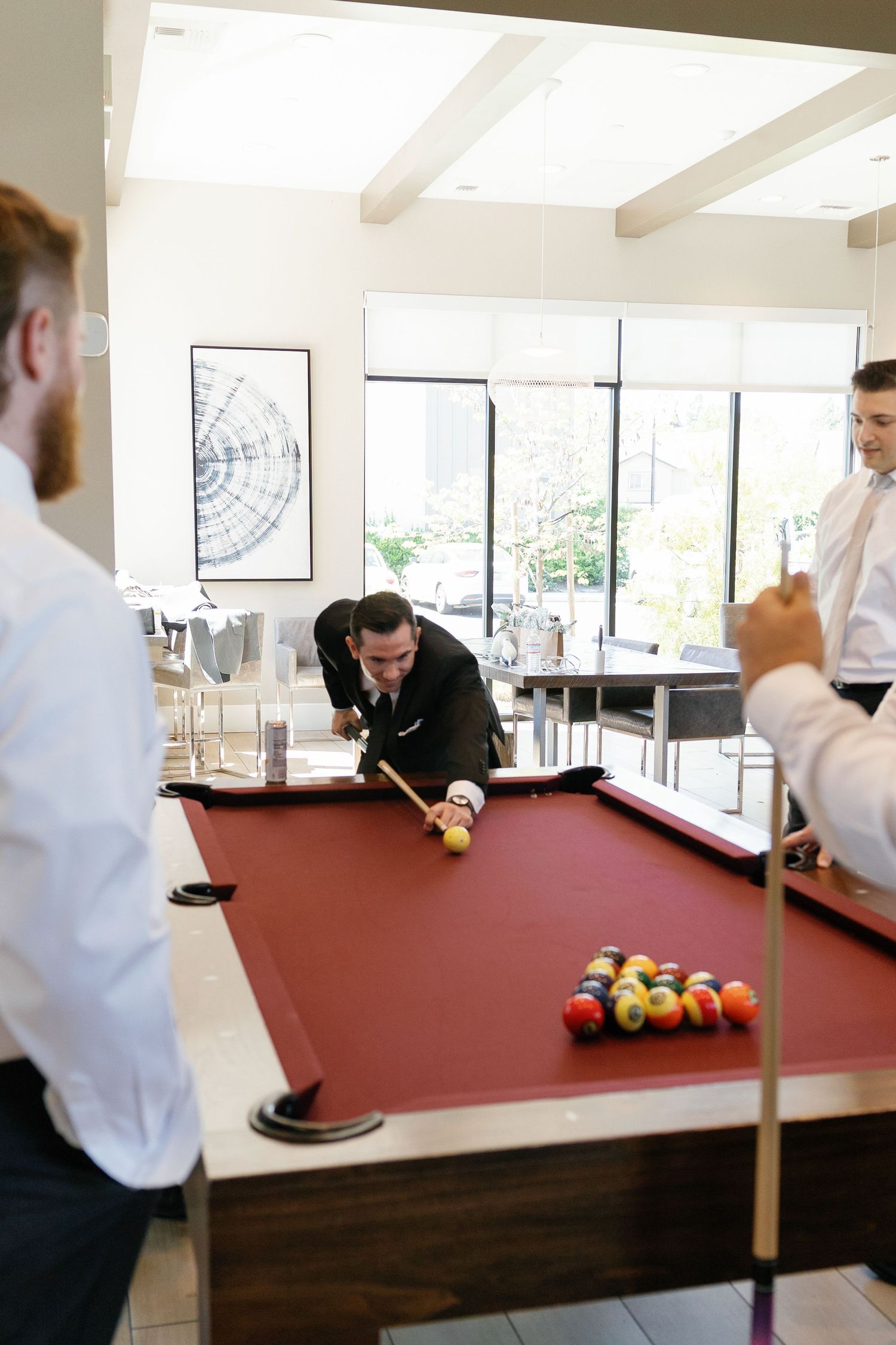 A sequence of pool billiards shots being played on a burgundy felt table in a bright room with windows.